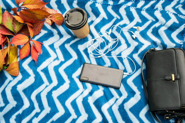 在户外放松在一个蓝色格子带耳机手机，纸杯与咖啡和秋叶，平躺图片下载