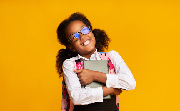 快乐的非洲裔美国女学生拥抱书在黄色的背景图片下载