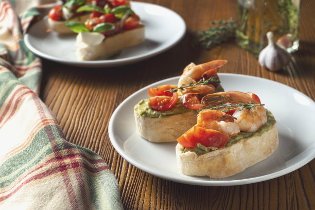 意式烤面包配虾、罗勒香蒜沙司和马苏里拉奶酪，放在木质背景的白色盘子上。意大利餐厅。俯视图食物照片图片下载