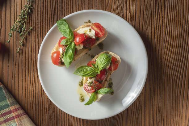 意式烤面包配樱桃番茄、罗勒、香蒜沙司和马苏里拉奶酪，配以木质背景的白色盘子。意大利餐厅。俯视图食物照片图片下载