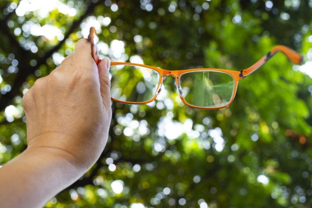 女人的左手拿着橙色眼镜在散景花园背景，近距离拍摄，选择性聚焦，形象，创意，文具概念图片下载