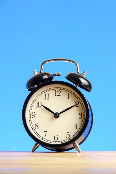 木制表面上的黑色闹钟映衬着蓝色的背景。图片下载