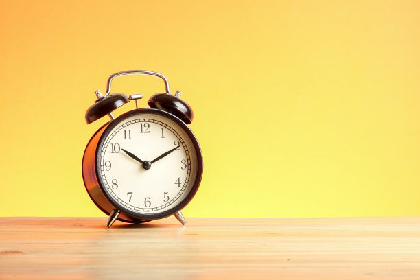 黑色的闹钟在木制的表面上映衬着黄色的背景。图片下载