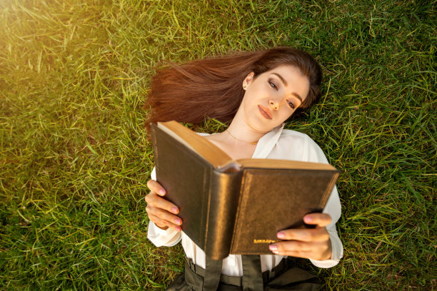 美丽的女人在草地上悠闲地看书图片下载