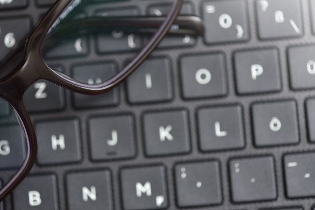 黑框眼镜放在笔记本电脑的键盘上，是视力丧失和疲劳的象征。特写镜头图片下载