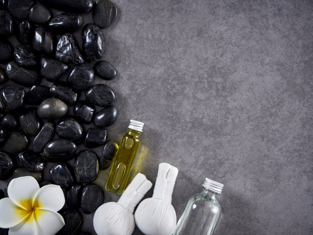 水疗按摩的概念。草药敷球，椰子油，身体乳液，滋养皮肤乳霜，香薰蜡烛，黑色鹅卵石在灰色大理石背景图片下载