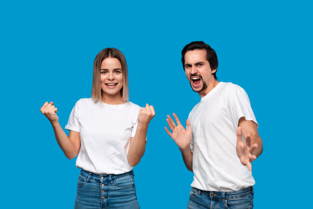 表达成功情感的幸福夫妇。年轻的金发女子和留着小胡子、穿着白色t恤和蓝色牛仔裤的大胡子男子获胜。模型孤立地站在蓝色背景上。图片下载