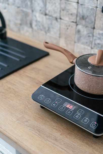 厨房炊具锅在小电炉和控制面板站在现代厨房的垂直照片。大理石墙面瓷砖和木制台面在模糊的背景上图片下载