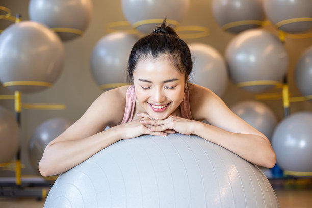 坐在体育馆里的女孩放松地抱着球。图片下载