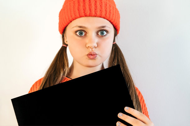 一个漂亮的女孩戴着一顶红帽子，睁着大大的眼睛，手里拿着一张黑纸图片下载