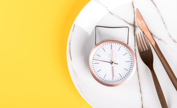 概念最小的“吃饭时间”。闹钟在一个白色的盘子上，在一个上黄色的背景。时髦的抽象风格。创造性的布局。前视图。平的。为文本复制空间。图片下载