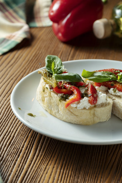 意式烤面包配甜椒、罗勒、香蒜沙司和马苏里拉奶酪，放在木质背景的白色盘子上。意大利餐厅。俯视图食物照片图片下载