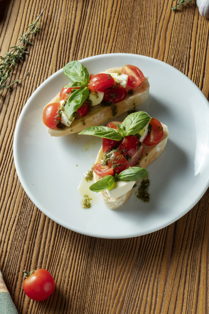 意式烤面包配樱桃番茄、罗勒、香蒜沙司和马苏里拉奶酪，配以木质背景的白色盘子。意大利餐厅。俯视图食物照片图片下载
