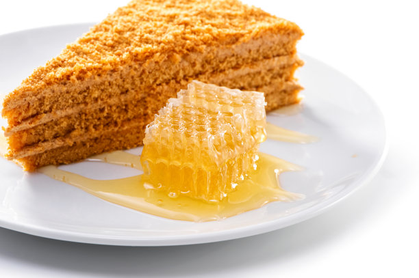 在白色背景上的一块蜂蜜奶油蛋糕旁边的蜂窝特写图片下载