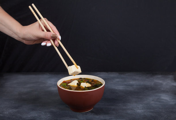 日本传统豆腐芝士汤。女性手拿筷子夹着豆腐奶酪。汤，蔬菜和海藻。图片下载