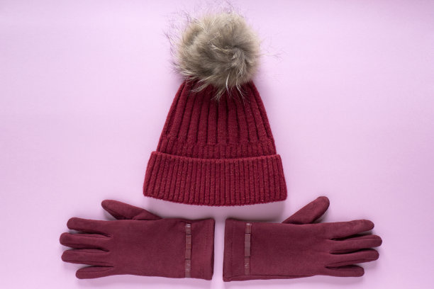 舒适温暖的冬季平躺与复印空间。深红色针织帽子毛皮绒球和酒红色手套在粉红色的背景图片下载