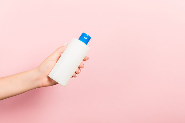 女性手捧霜瓶隔离乳液。女孩给管化妆品粉红色的背景图片下载