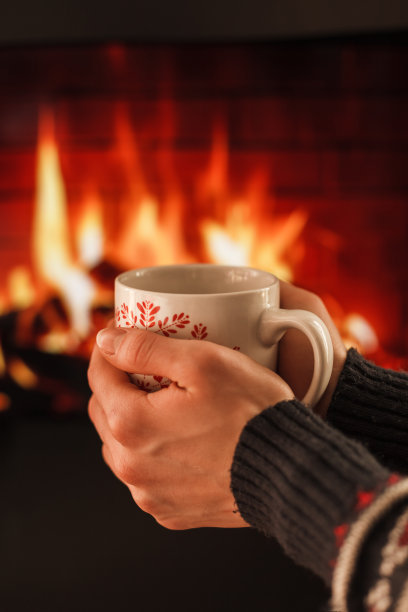 两只手捧着一个温暖的杯子在壁炉前图片下载