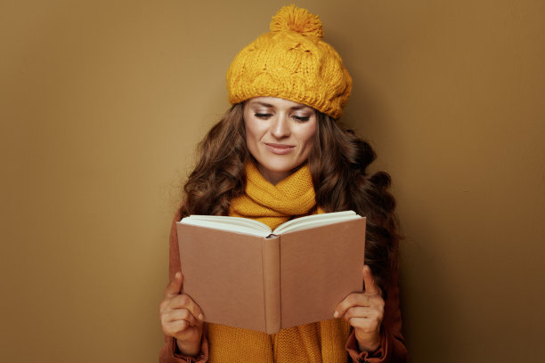 快乐的年轻女子在米色的背景下看书图片下载