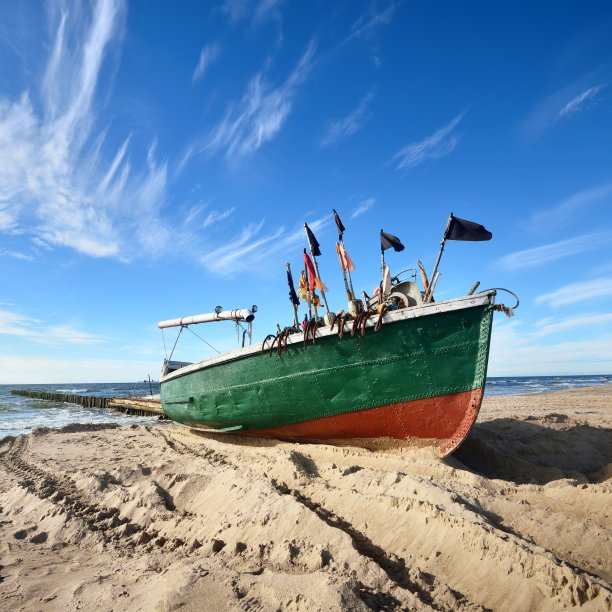 在一个晴朗的阳光明媚的日子里，一艘挂着旗帜的绿色巡逻艇停在海滩上图片下载