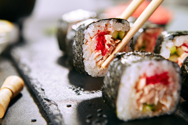 在日本餐馆用筷子吃寿司卷的微距镜头。吃一份寿司卷配米饭、炸鲑鱼、飞鱼鱼子酱、黄瓜和辣酱图片下载