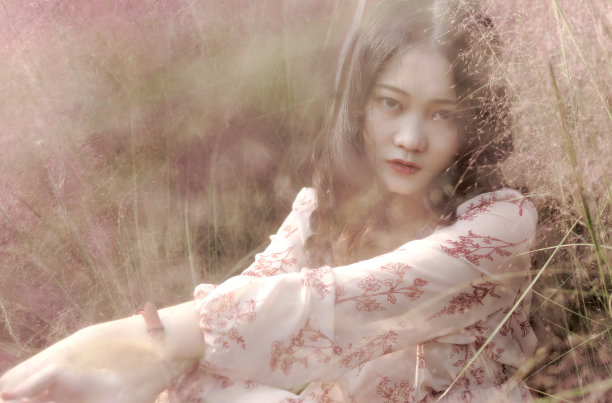 一个美丽的中国年轻女子的肖像穿着粉红色的裙子坐在粉红色的头发多的领域，看着和微笑的相机，复古模式。素材图片