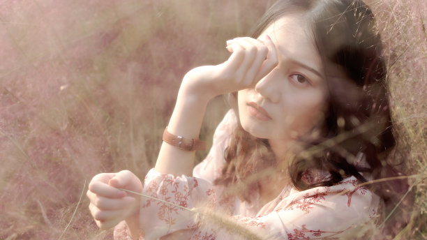 一个美丽的中国年轻女子的肖像穿着粉红色的裙子坐在粉红色的头发多的领域，看着和微笑的相机，复古模式。素材图片