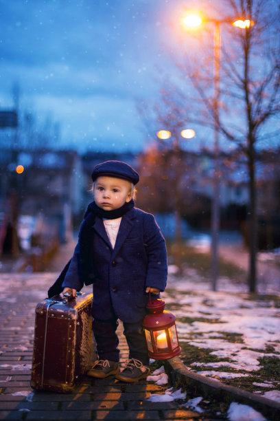 蹒跚学步的男孩站在楼梯上，提着灯笼和旧行李箱，这是布拉格雪夜的街景图片下载