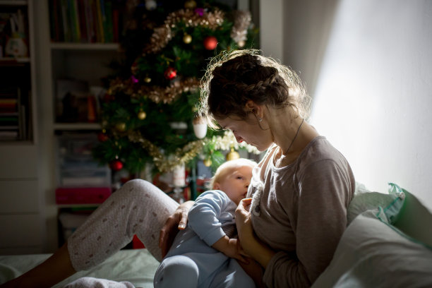 年轻美丽的母亲，在昏暗的灯光下给她的新生儿喂奶。妈妈母乳喂养孩子图片下载