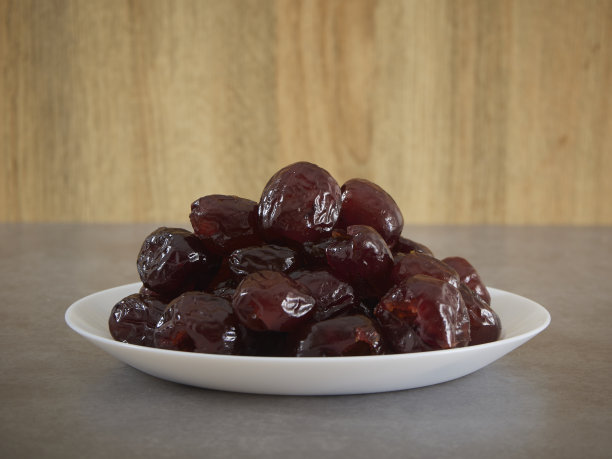 灰色大理石桌上白色的盘子里放着香甜的枣干。图片下载