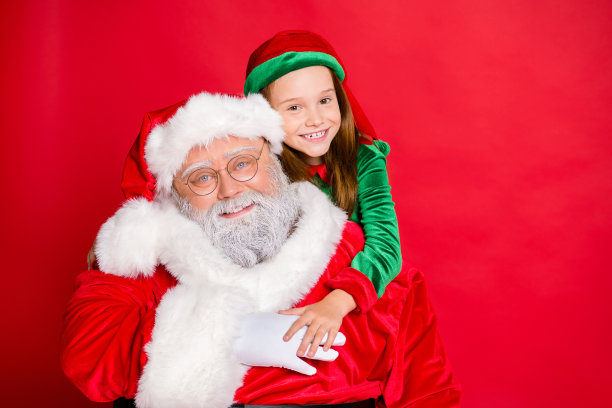 近距离的照片，迷人的小精灵助手在绿色的帽子头饰拥抱她的滑稽圣诞老人戴眼镜孤立在红色的背景图片下载