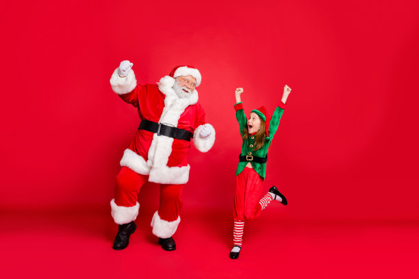 兴奋的圣诞老人小精灵的全身照片头戴红发白色发型举起拳头尖叫是的庆祝派对穿绿色服装孤立在红色背景图片下载