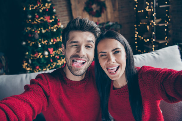 近距离的照片，两个funky疯狂浪漫的人在圣诞节假期坐在沙发上自拍愚弄新年照明室内图片下载