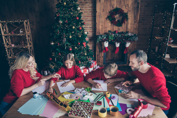 大家庭的照片，爸爸，妈妈，姐姐，哥哥一起过圣诞节早上，父母协助写圣诞老人祝福信，坐在桌子里，在室内穿红色毛衣图片下载