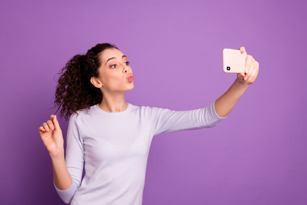 照片欢快的卷发时尚时尚可爱甜美的千禧女孩亲吻她的新电话穿着毛衣的头发孤立在紫罗兰柔和的颜色背景图片下载