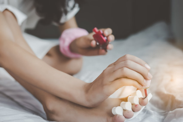 美丽的女人用红色指甲油涂她美丽的脚趾甲，在早上在家修脚，笑脸。迷人的美丽的女人喜欢涂她的指甲，足疗，她感到幸福图片下载