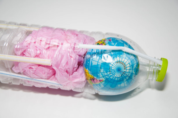 一个地球仪，塑料袋和塑料瓶中的塑料管，这是来自塑料的全球环境的概念。图片下载