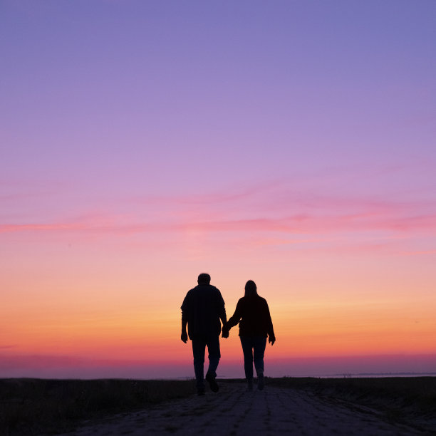 男人和女人的剪影手牵着手走在缤纷的日落图片下载