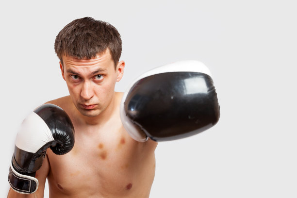 一名戴着拳击手套的男子在一场打斗和拳击中被刺伤，他的身体和面部都有瘀伤，背景是白色的。体育和武术。图片下载