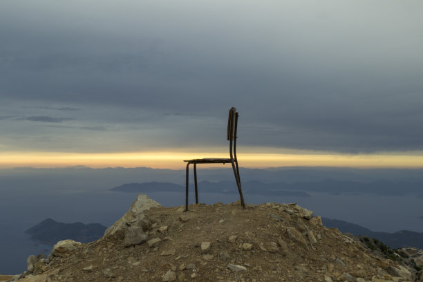 海面上的日落，灿烂的阳光透过云层倾泻而下。山顶上的一把椅子图片下载