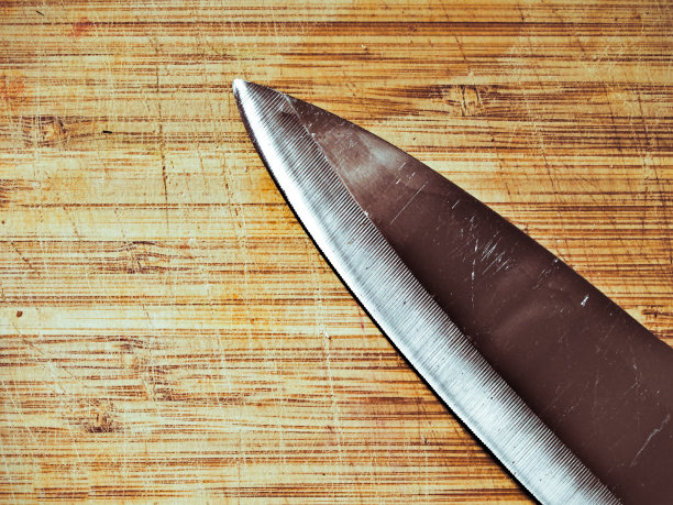 大厨师刀细节与边缘指向木质砧板表面。黑暗的效果。图片下载