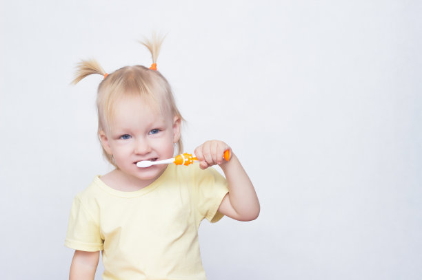 金发碧眼的小女孩梳着辫子，一边刷牙一边看着镜头，白色的背景，复制空间，白种人图片下载