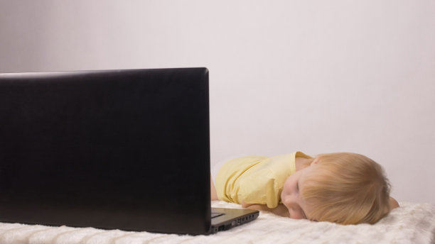 小女孩躺着，看着电脑屏幕，笔记本电脑，白色的背景，看卡通片图片下载