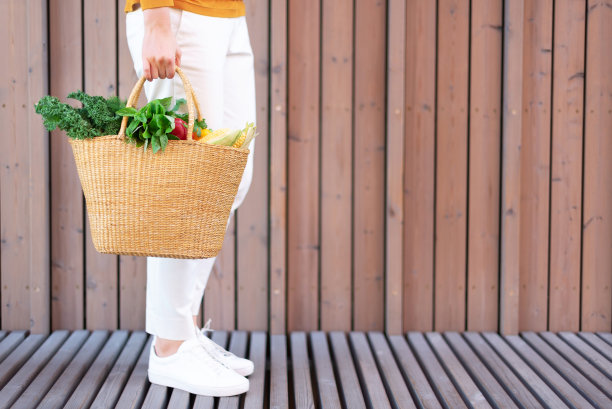 小女孩拿着草篮，里面装着蔬菜，产品没有塑料袋，木质背景。零浪费，无塑料的概念。可持续的生活方式。横幅。图片下载