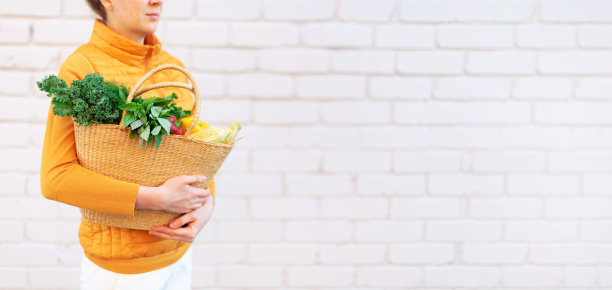 女孩抱着草编篮，配以健康有机蔬菜，砖砌背景，复制空间。秋天的收获。零浪费，无塑料的概念。可持续的生活方式。感恩节图片下载