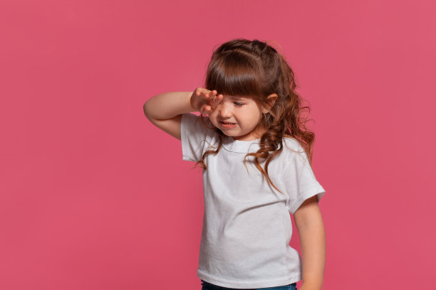 特写的一个小女孩穿着白色t恤摆姿势，以粉红色的工作室背景。真诚的情感概念图片下载