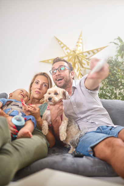 年轻的父母和小男孩和小狗一起看电视。图片下载