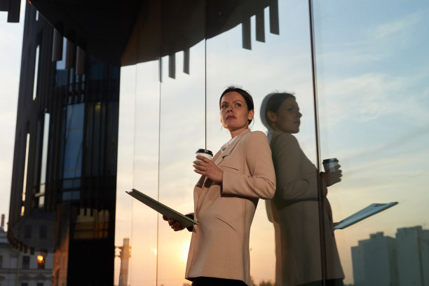 体贴自信迷人的商务女士在优雅的夹克站在现代建筑和喝咖啡，同时分析报告图片下载