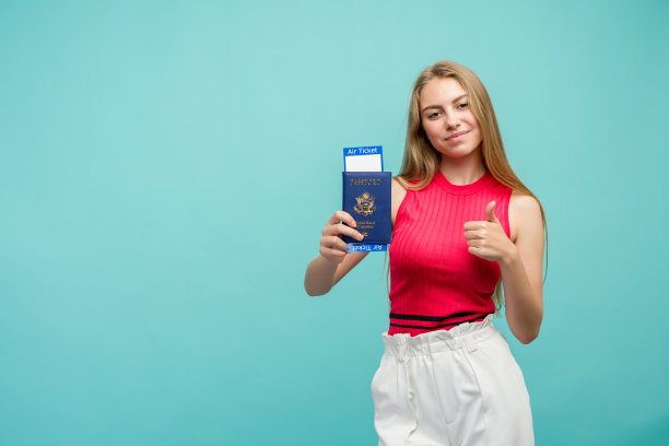 一名年轻漂亮的女学生拿着护照和门票的照片。孤立在明亮的蓝色背景。图片下载