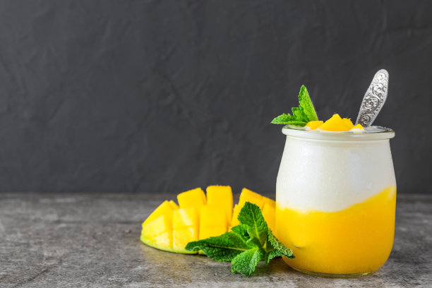 芒果果酸奶与新鲜薄荷在一个玻璃杯和勺子在黑色混凝土背景。健康的早餐图片下载